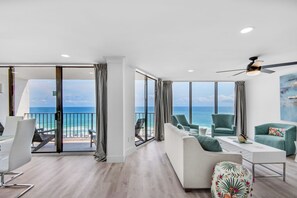 A modern living room with a balcony overlooking the ocean, furnished with a sofa, chairs, and a coffee table.