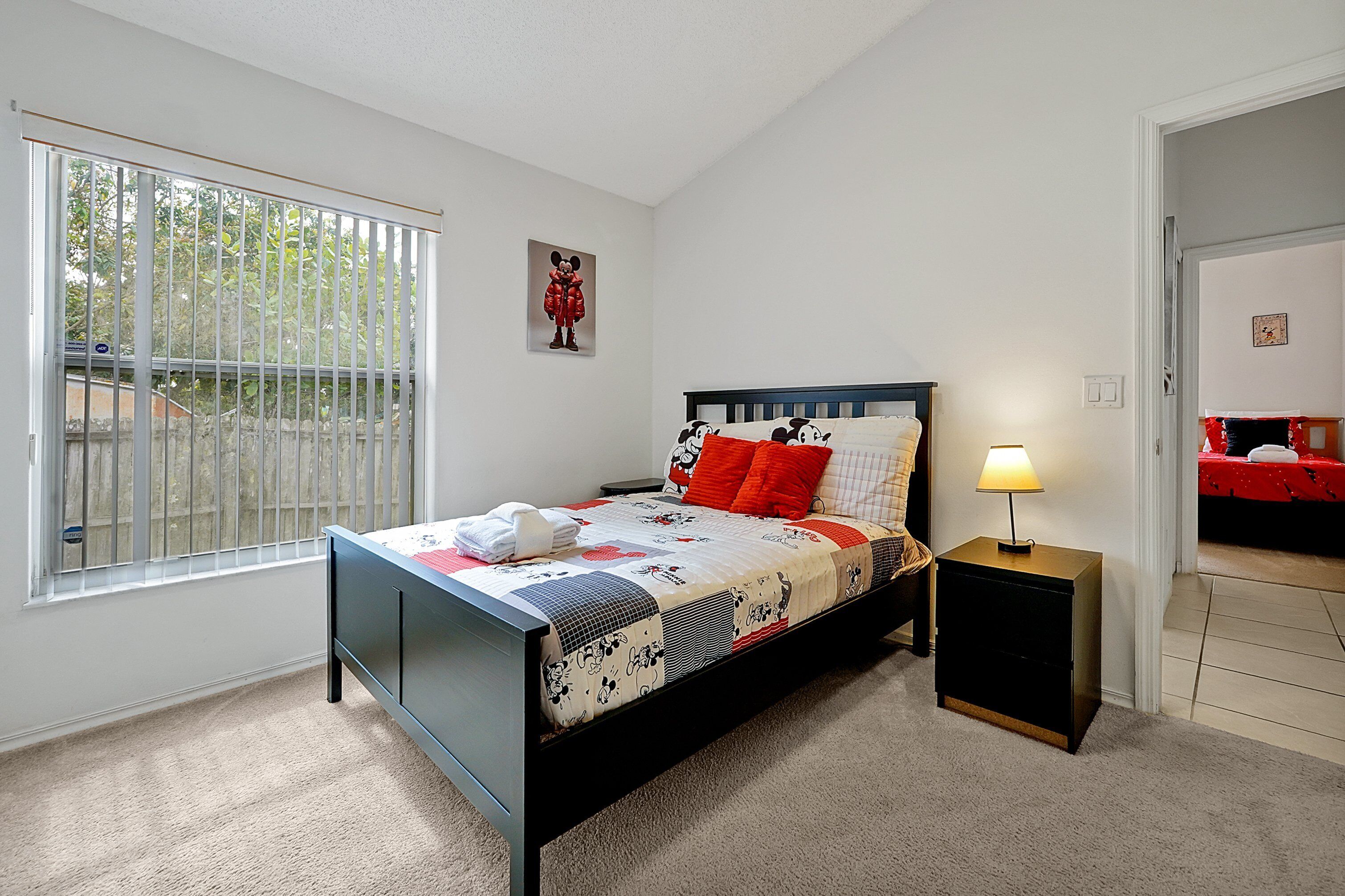 Une chambre à coucher comprenant un lit, une table de chevet, une fenêtre avec des stores et une porte donnant sur une autre pièce.