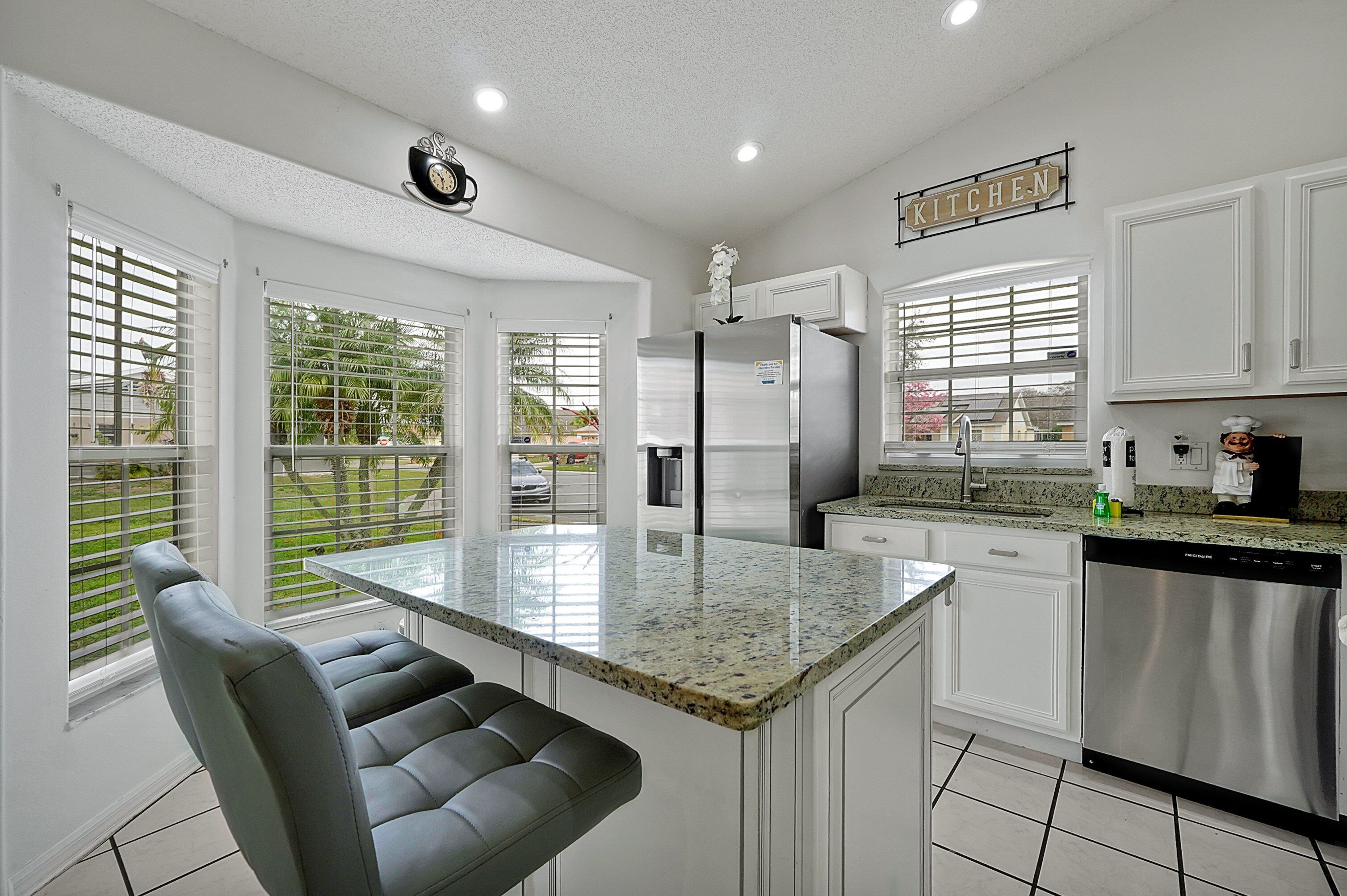 A modern kitchen with white cabinetry, a stainless steel refrigerator, and a granite countertop.