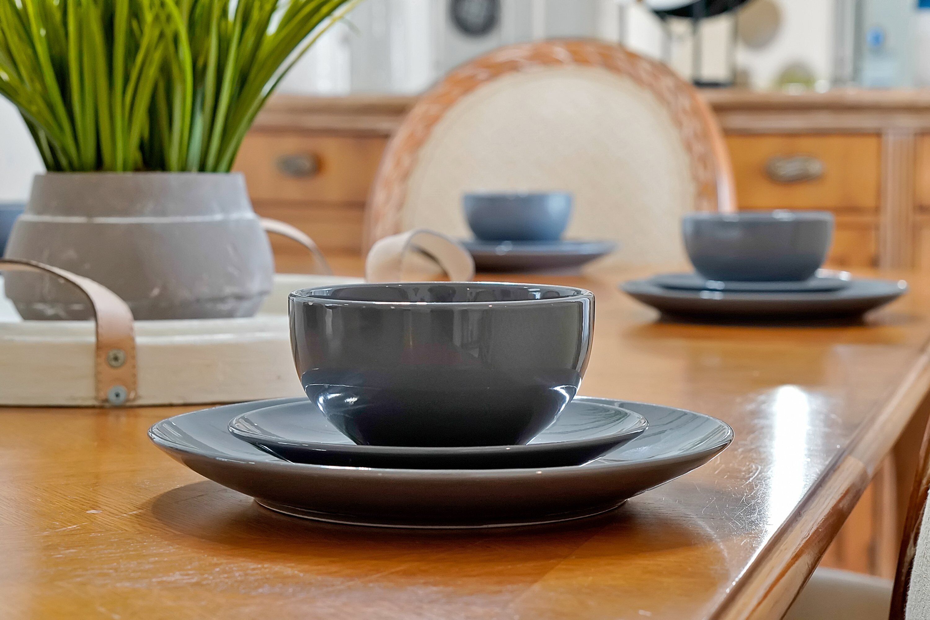 Een eettafel met een donkere keramische kop en schotel, een potplant en een houten stoel.
