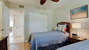 A bedroom with a bed, a nightstand with a lamp, a wall clock, and a beach-themed painting.