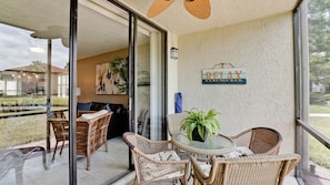Un balcon fermé par des parois de verre, agrémenté de meubles en osier, d’une table en verre et d’une pancarte « RELAX » accrochée au mur.