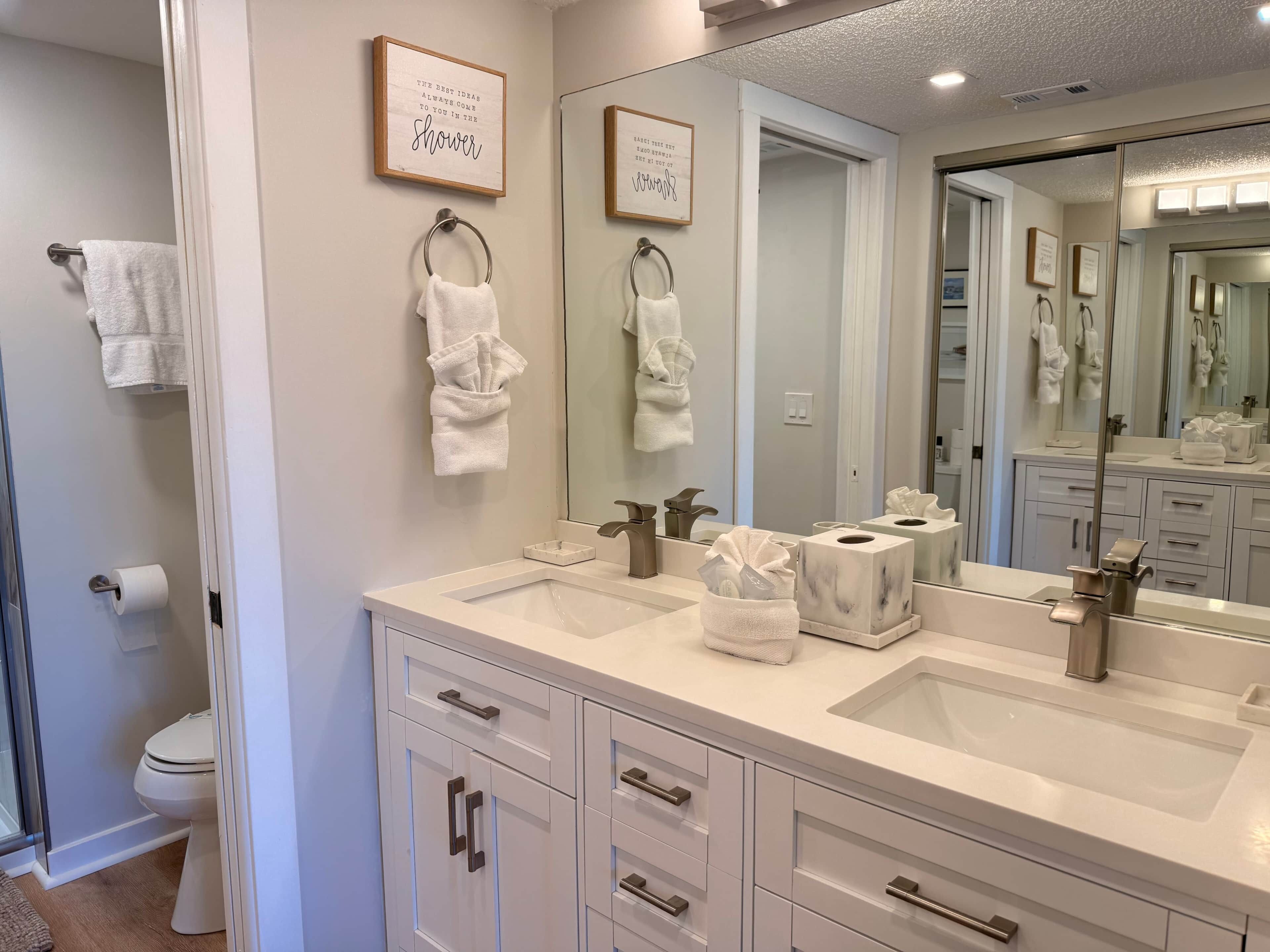 A bathroom with two sinks, a toilet, a mirror, and towels.