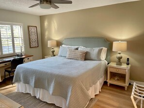 Une chambre à coucher comprenant un lit, deux tables de chevet, un bureau, une chaise et un ventilateur de plafond.