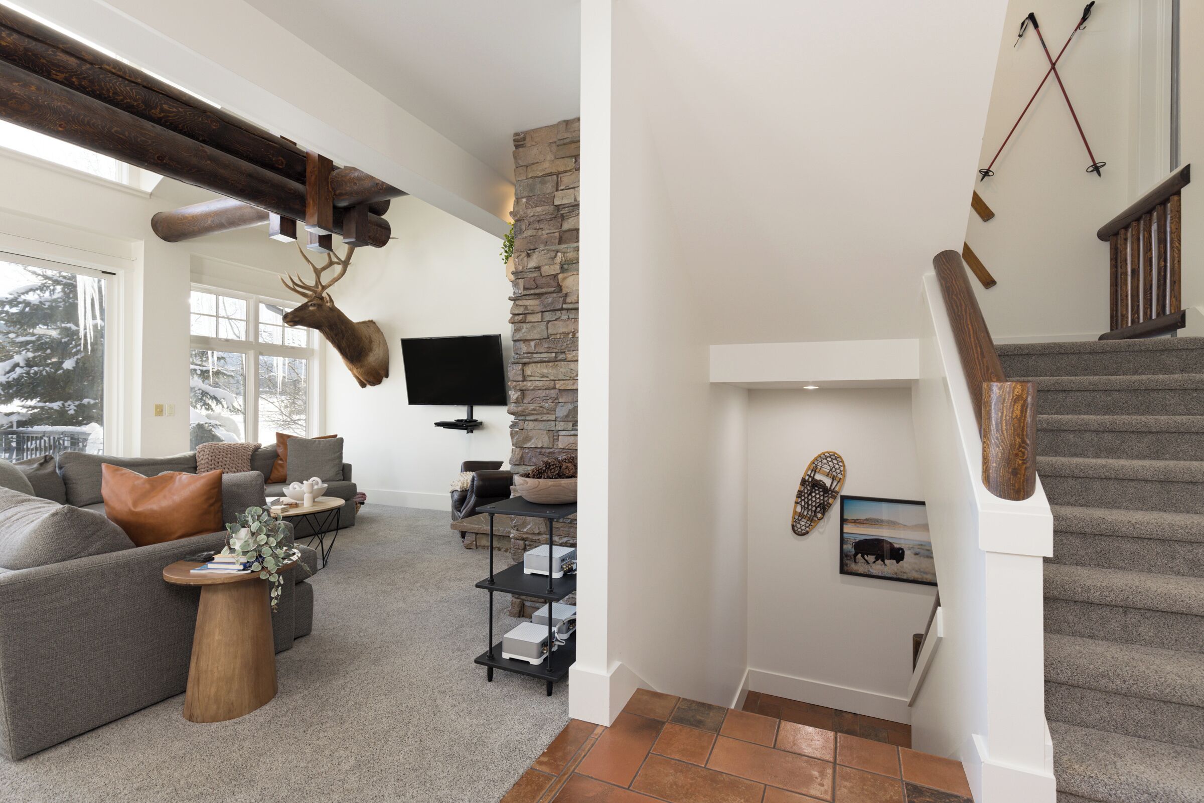 A modern living room with a stone accent wall, a mounted deer head, and a staircase with wooden railings.
