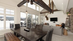 Un vaste espace de vie comprenant une grande table à manger en bois, des sièges confortables, une cheminée en pierre et une tête de cerf fixée au mur.