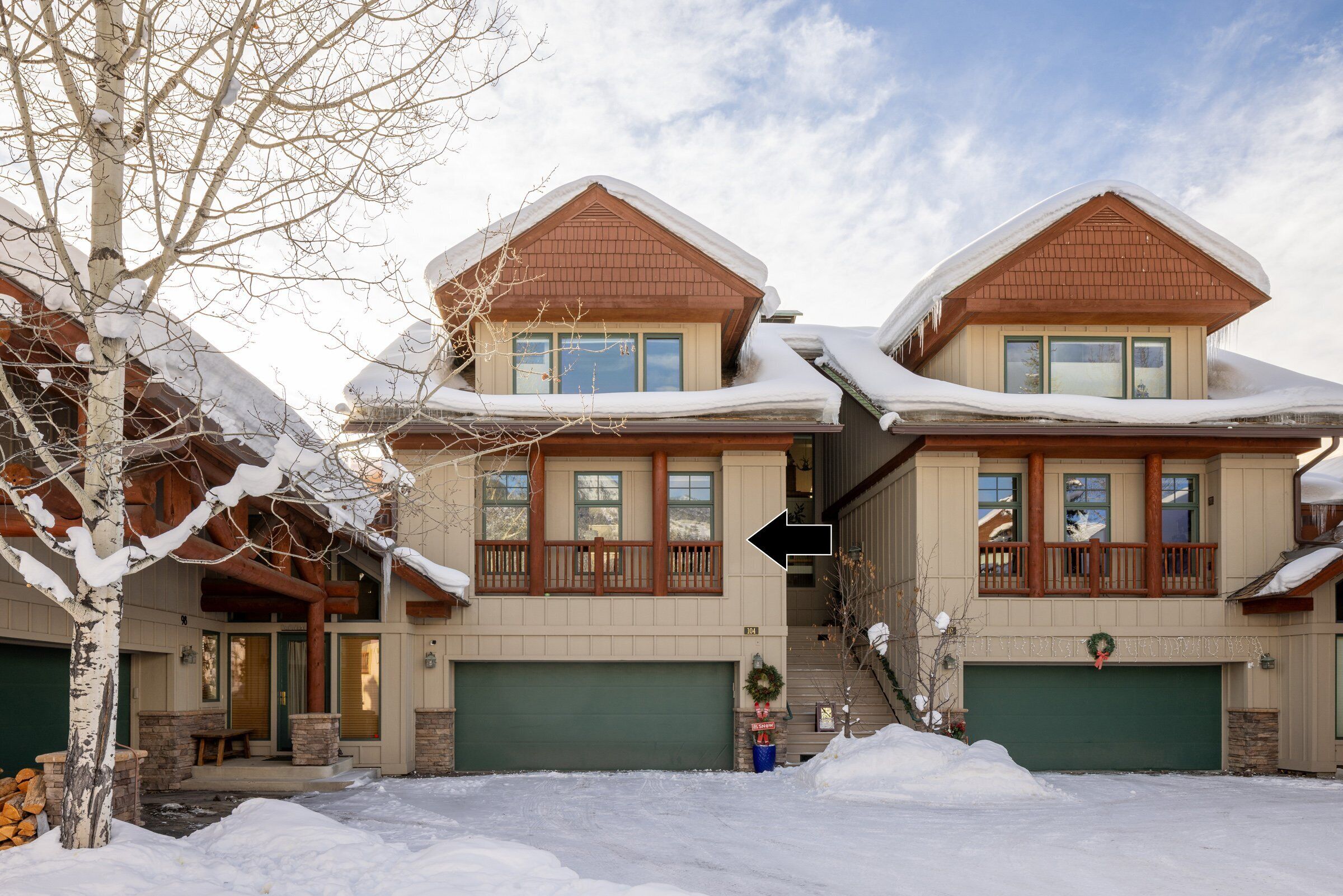 Une maison à deux étages avec un garage vert, un porche avant couvert et un toit recouvert de neige.