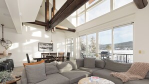 Un salon moderne avec un grand canapé d’angle gris, une table basse en bois et une vue sur un paysage enneigé par de grandes fenêtres.