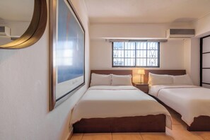 A hotel room with two beds, a large window with decorative bars, a wall-mounted air conditioner, and a framed picture above the left bed.