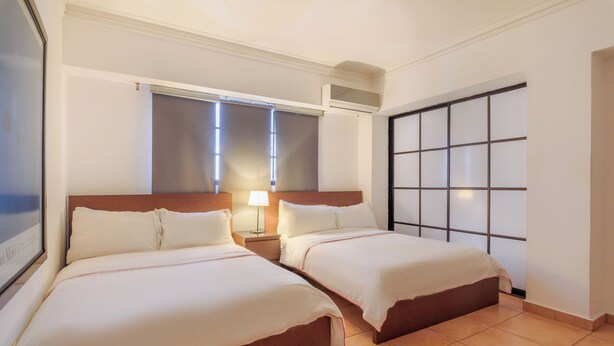 A hotel room with two beds, a large window with blinds, a wall-mounted air conditioner, and a sliding door with a grid pattern.