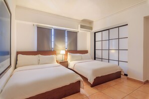 Camera d'albergo con due letti, un'ampia finestra con tende, un condizionatore d'aria a parete e una porta scorrevole con motivo a griglia.