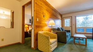 A cozy living room with a wooden wall, a green carpet, a yellow armchair, a grey sofa, and a small wooden table. - Ski In/Out Right to the Elk Chairlift (Fernie)