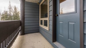 A corner of a building with a dark blue exterior, a wooden porch, and a window with a white frame. - Ski In/Out Right to the Elk Chairlift (Fernie)