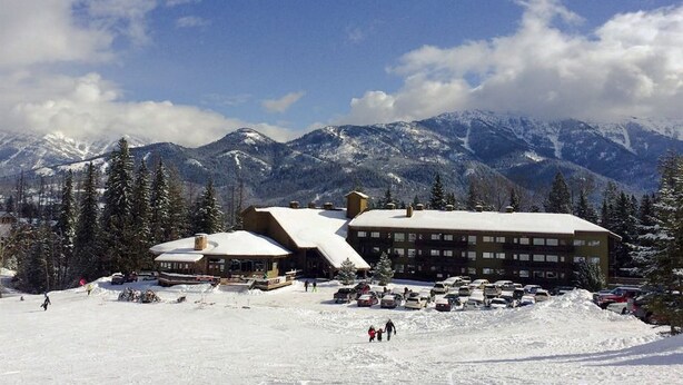 A ski resort with buildings, a parking lot, and snow-covered mountains in the background. - Ski In/Out Right to the Elk Chairlift (Fernie)