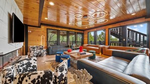 A spacious living area with a fireplace, leather sofas, and a wooden ceiling with circular light fixtures.