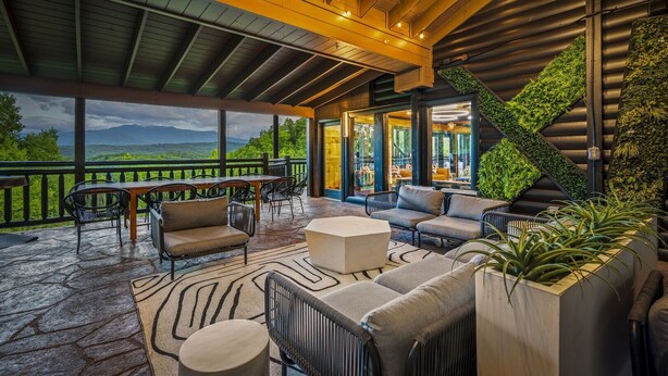 A covered outdoor seating area with a view of the mountains, furnished with sofas, chairs, and tables.
