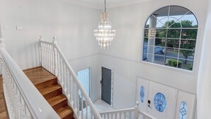 A grand staircase with a chandelier, a large arched window, and decorative moldings. - Holiday Inn (Parkinson)