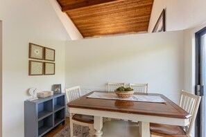 A dining area with a wooden table, white chairs, a dark blue console, and wall art. - The Blue Pearl - 2 minute walk to the beach! (Del Mar)