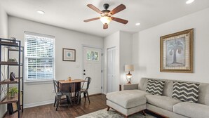 A modern living room with a sectional sofa, a dining table with chairs, a ceiling fan, and a large window with blinds. - Charming villa steps from the water in beautiful Pensacola (Pensacola)