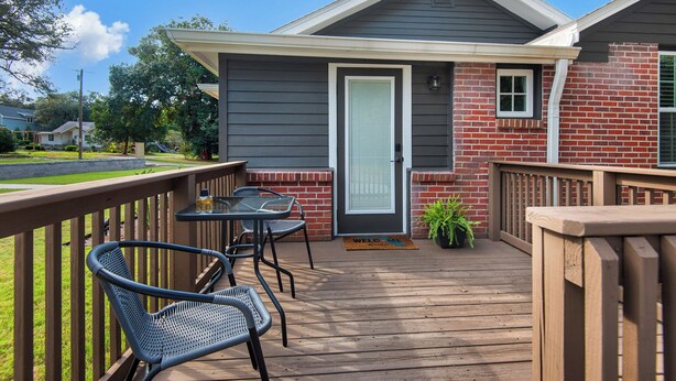 A wooden deck with two chairs and a small table, a door with a window, and a brick wall. - Charming villa steps from the water in beautiful Pensacola (Pensacola)