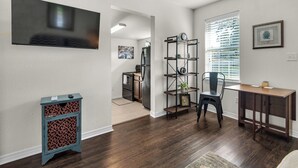 A modern living room with hardwood flooring, a TV mounted on the wall, a desk with a chair, and a bookshelf. - Charming villa steps from the water in beautiful Pensacola (Pensacola)