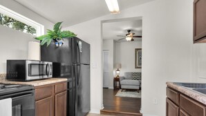 A kitchen with a black refrigerator, a microwave, and a stove. There is a plant on the refrigerator and a ceiling fan in the adjacent living room. - Charming villa steps from the water in beautiful Pensacola (Pensacola)