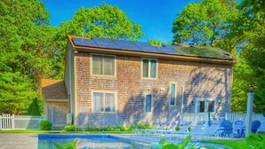 A house with a brick exterior, a swimming pool, and blue hydrangea flowers in the foreground. - Overlook Poolside Getaway Heated Pool (May - Oct 20th) (East Falmouth)