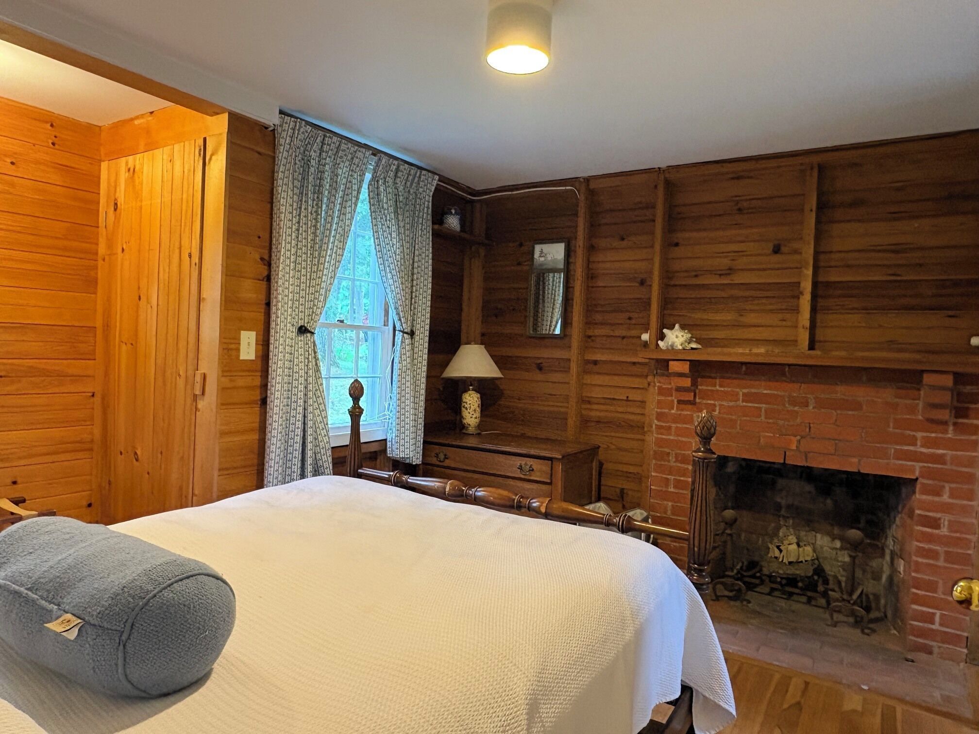 Ein Zimmer aus Holz mit einem Bett, einem Kamin und einem Fenster mit Vorhängen.