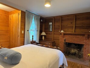 Ein Zimmer aus Holz mit einem Bett, einem Kamin und einem Fenster mit Vorhängen.