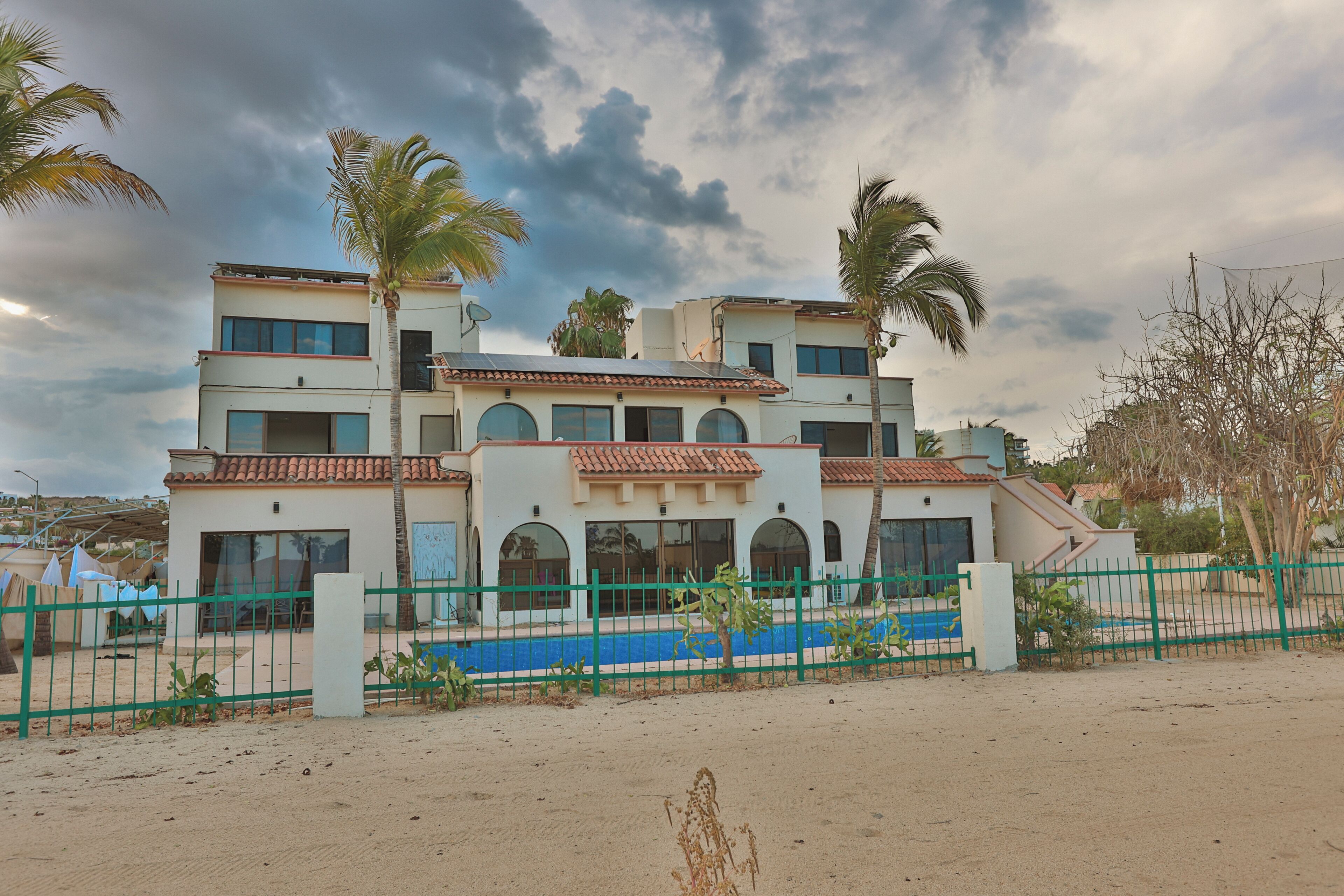 A multi-story building with a flat roof, large windows, and a blue swimming pool in the foreground.