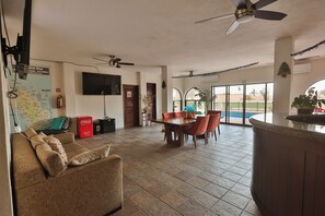 A spacious living area with a dining table, sofas, and a TV mounted on the wall. - Hostal Hab 12, Campo de Golf, En Zona Hotelera, Barra, Playa (San José del Cabo)