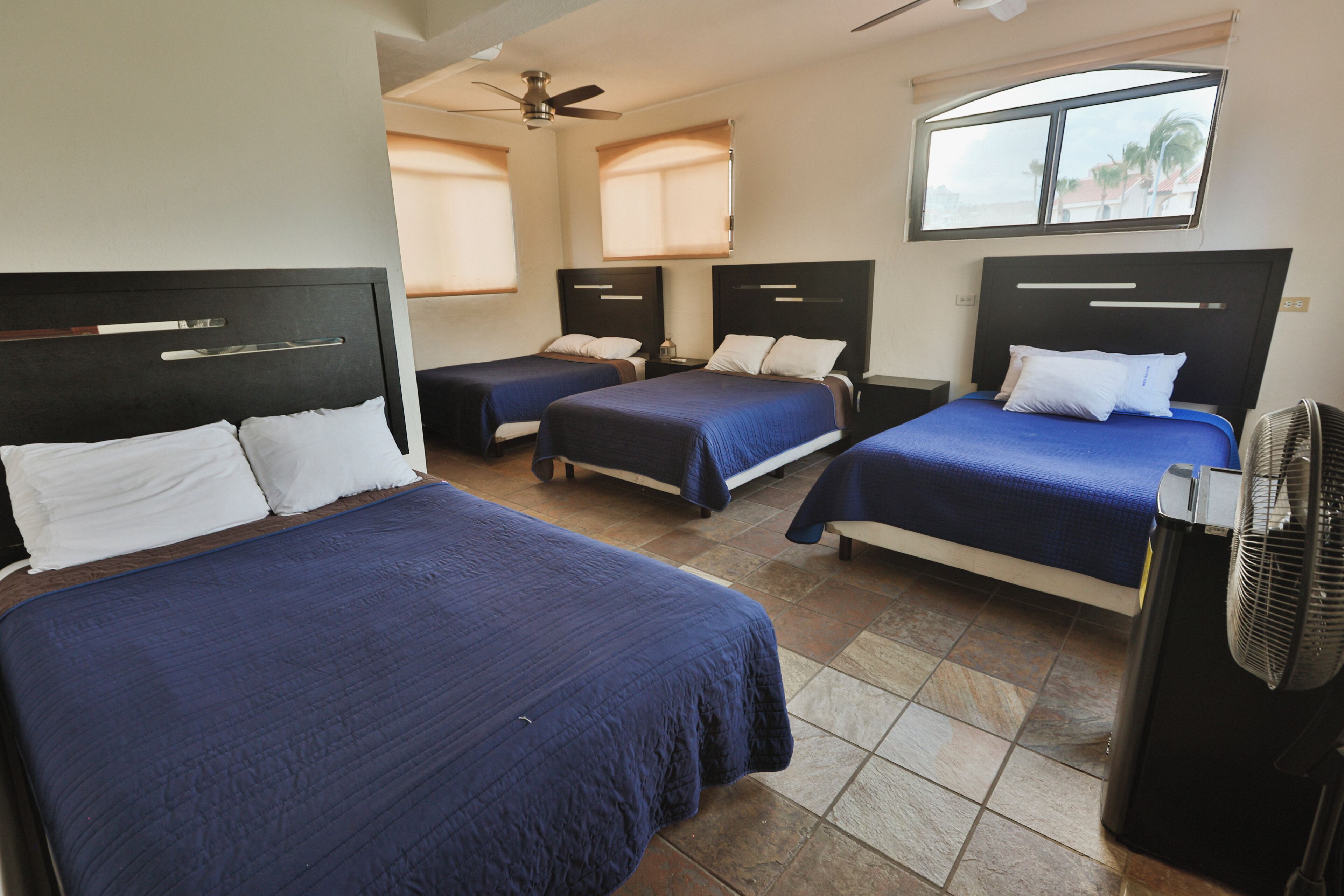 A hotel room with three single beds, a ceiling fan, and a window with a view.