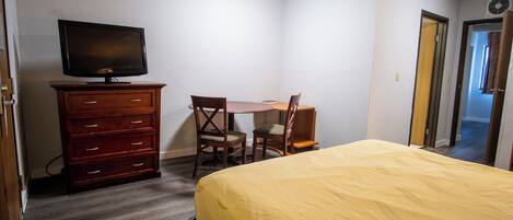 A bedroom with a bed, a dresser, a television, and a desk with two chairs.