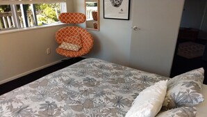 A bedroom with a floral-patterned bedspread, a white pillow, and an orange cushion on a chair.