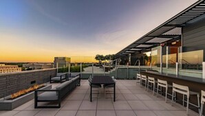 A rooftop terrace with outdoor seating, a bar area, and a view of the city skyline. - Tysons 2BR | Balcony, Pool & Fitness (McLean)