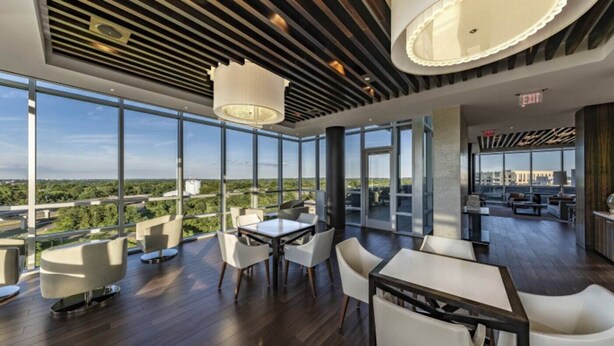 A modern interior with a large dining area, high ceilings, and expansive windows offering a city view. - Tysons 2BR | Balcony, Pool & Fitness (McLean)