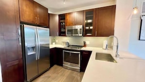 A modern kitchen with stainless steel appliances, wooden cabinets, and a white countertop. - Tysons 2BR | Balcony, Pool & Fitness (McLean)