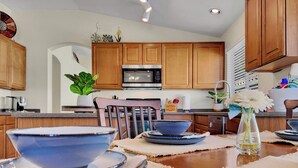A modern kitchen with wooden cabinets, a microwave, and a dining table set with blue dishes and a vase with flowers. - 3BR w private yard, grill, garden view (San Tan Valley)
