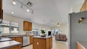 A modern kitchen with wooden cabinets, a central island, and a refrigerator. - 3BR w private yard, grill, garden view (San Tan Valley)