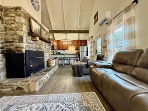 A cozy living room with a stone fireplace, leather sofa, and a kitchen in the background.