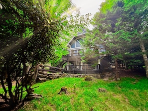 A house with a balcony, surrounded by trees and a grassy area.