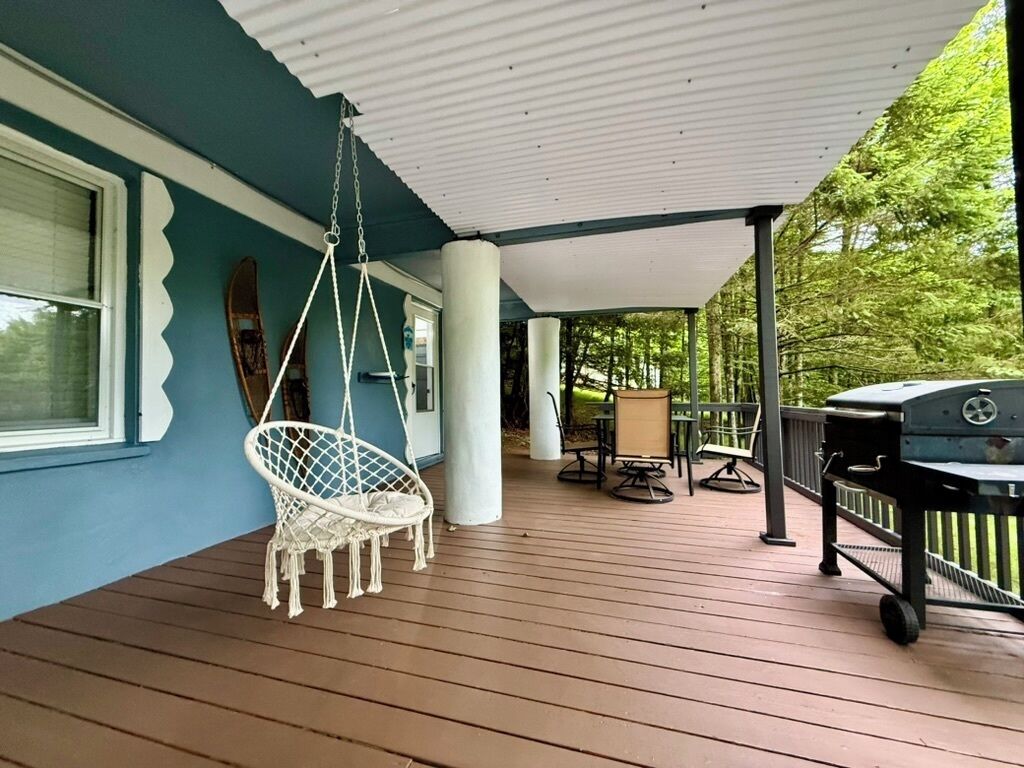 Eine überdachte Veranda mit Hängesessel, Grill und Tisch mit Stühlen.
