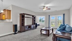 Een ruime woonkamer met een grote flatscreen-televisie, een plafondventilator en een balkon met uitzicht.