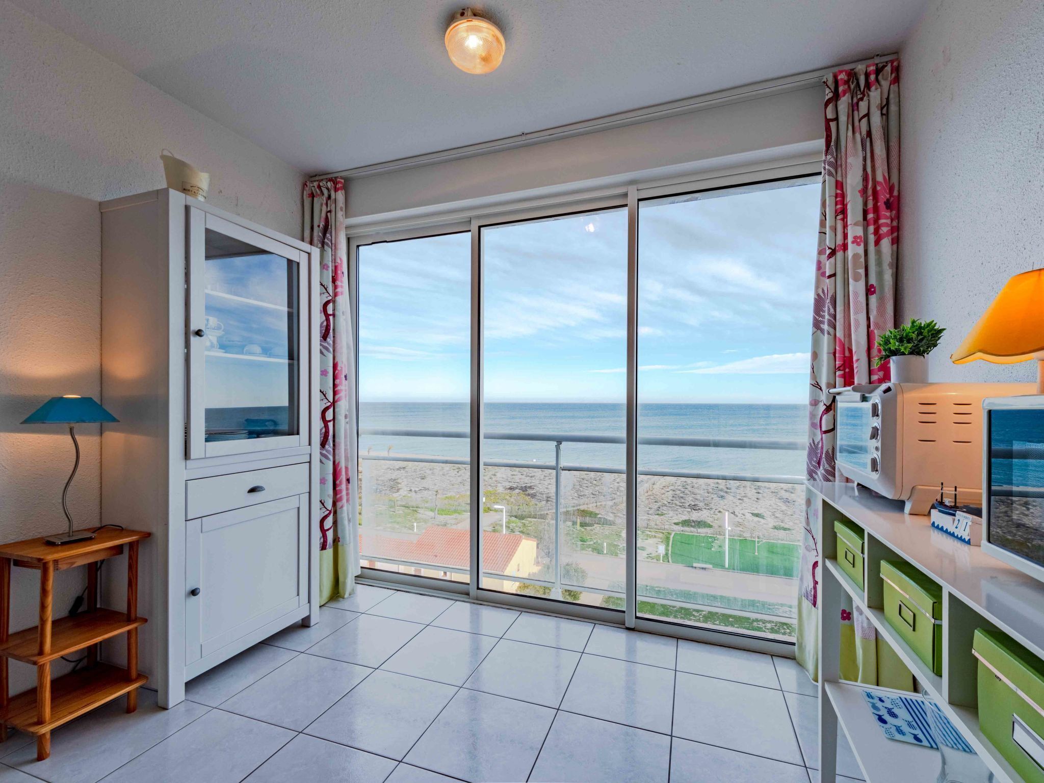 A balcony with a view of the sea, a white cabinet, a wooden shelf, and a green storage unit.