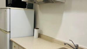 Una cocina con armarios blancos, un lavamanos de acero inoxidable, un microondas y un refrigerador.