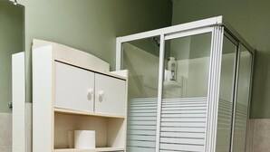 Un baño con inodoro, un armario con estantes y una cabina de ducha de vidrio.