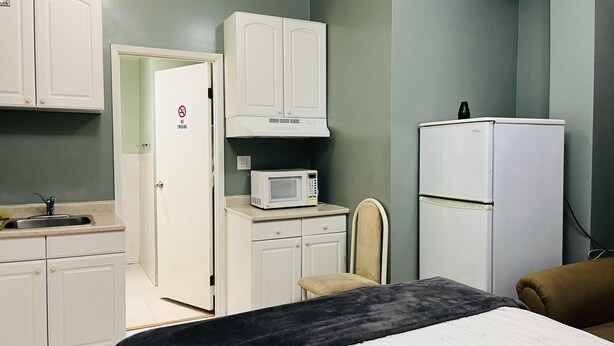 Una habitación de hotel compacta con kitchenette, una cama, una silla y un refrigerador.