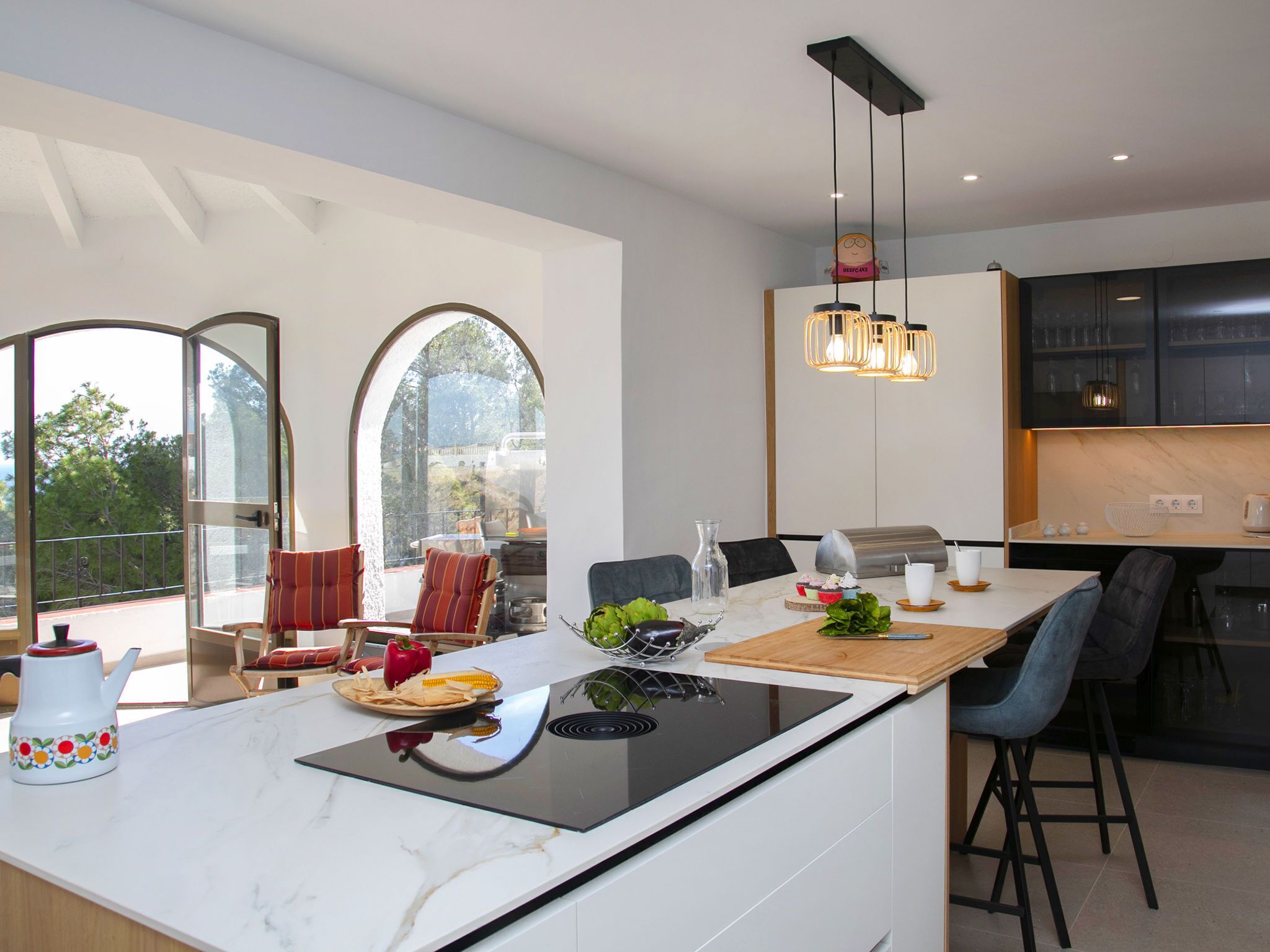 Een moderne keuken met een centraal eiland, een eethoek en grote ramen.
