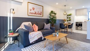 Una sala de estar moderna con sofá, mesa de centro y comedor. Se ve una cocina al fondo.