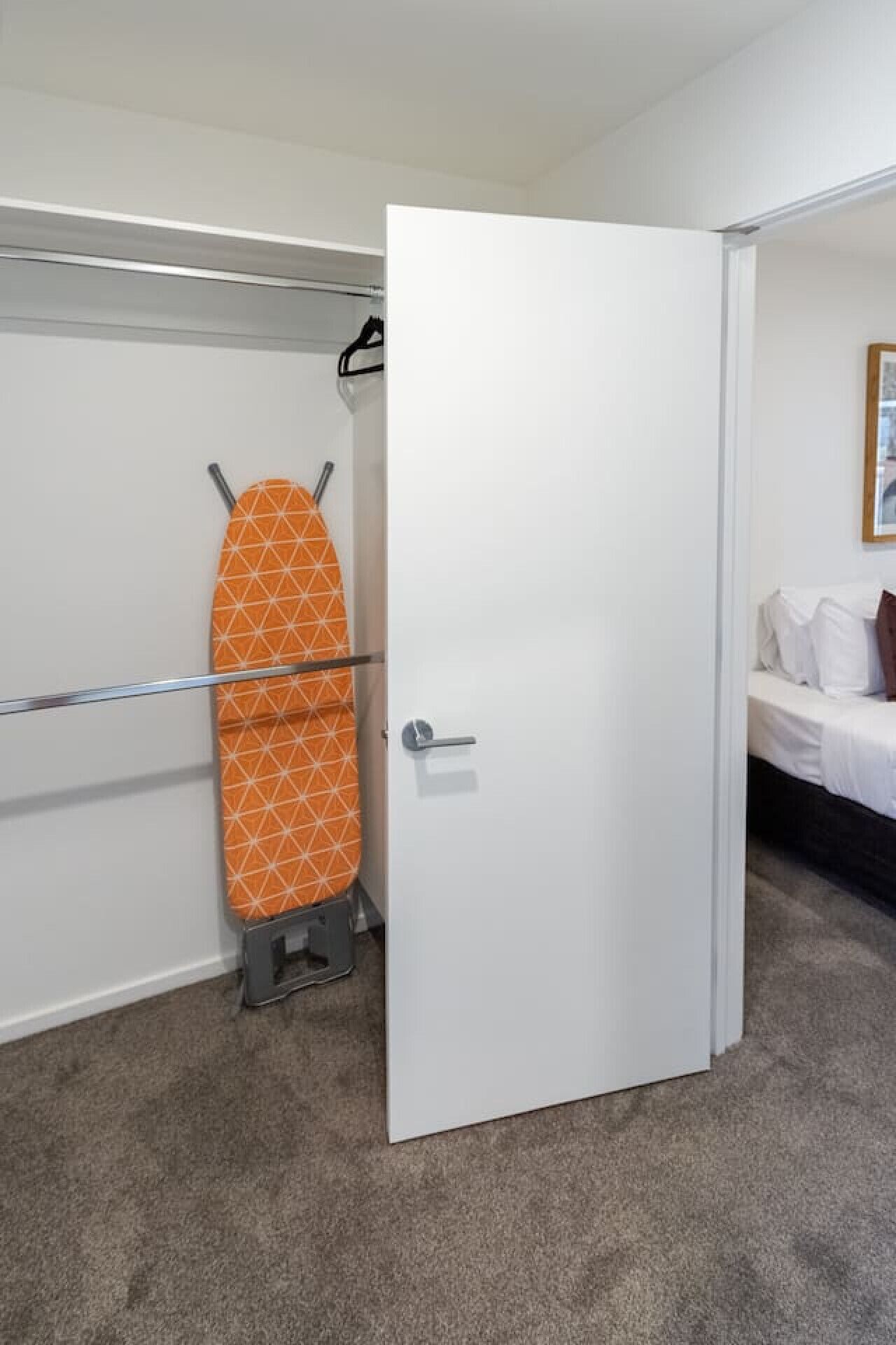 Un dormitorio con cama, un armario con tabla de planchar y una puerta.